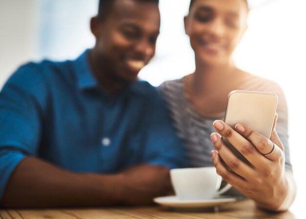 Der Kennenlernteil des Dates Aufnahme eines jungen Mannes und einer jungen Frau, die gemeinsam ein Mobiltelefon bei einem Date in einem Café benutzen