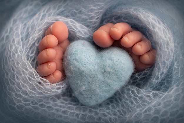 Der kleine Fuß eines neugeborenen Babys. Weiche Füße eines Neugeborenen in einer hellblauen Decke. Nahaufnahme von Zehen, Fersen und Füßen eines Neugeborenen. Gestricktes blaues Herz in den Beinen eines Babys. Makrofotografie im Studio.