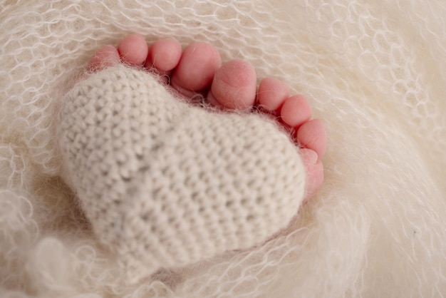 Der kleine Fuß eines neugeborenen Babys Weiche Füße eines Neugeborenen in einer weißen Wolldecke Nahaufnahme der Zehen, Fersen und Füße eines Neugeborenen Gestricktes Herz in den Beinen des Babys Makro-Studiofotografie