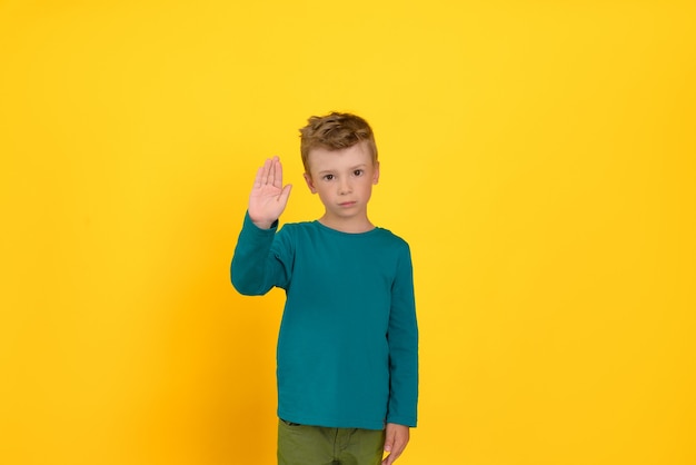 Der kleine Junge auf gelbem Hintergrund zeigt mit der Hand Halt, er hat einen traurigen Ausdruck im Gesicht.