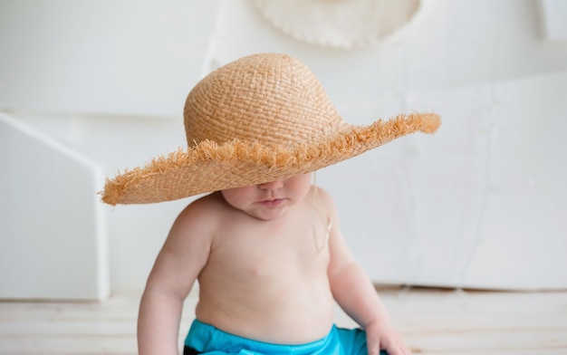 Der kleine Junge bedeckte sein Gesicht mit einem Strohhut auf einer weißen Oberfläche mit Platz für Text