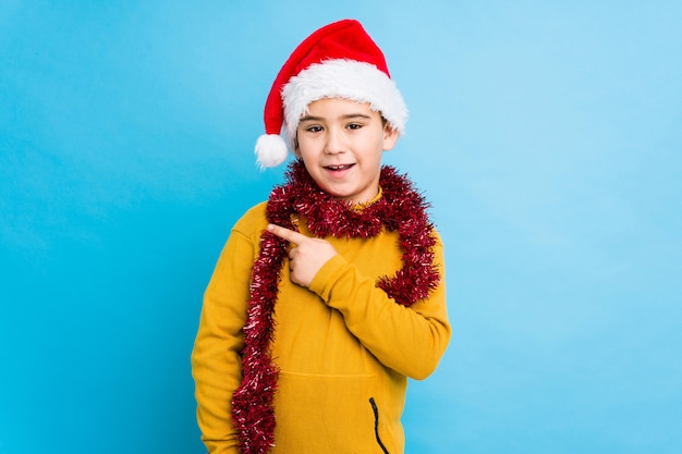 Der kleine Junge, der den Weihnachtstag trägt einen Sankt-Hut feiert, lokalisierte das Lächeln und beiseite zeigen und zeigte etwas an der Leerstelle.