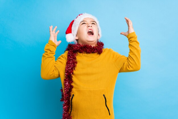 Der kleine Junge, der den Weihnachtstag trägt einen Sankt-Hut feiert, lokalisierte das Schreien zum Himmel und schaute oben, frustriert.