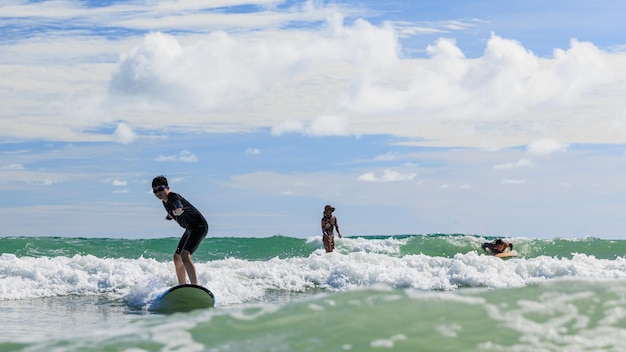 Foto der kleine junge, der eine schwimmbrille trägt, steht auf einem weichen brett, während er das surfen in der anfängerklasse übt