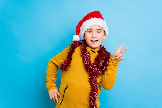 Der kleine Junge, der Weihnachtstag einen Sankt-Hut tragend feiert, lokalisierte das frohe und sorglose Zeigen eines Friedenssymbols mit den Fingern.