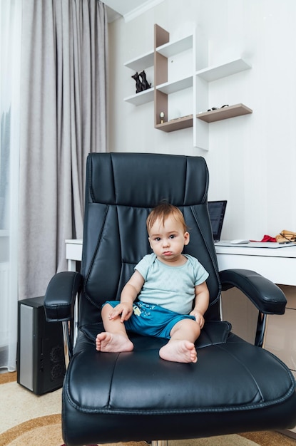 Der kleine Junge, der zu Hause auf einem Bürostuhl sitzt Baby-Chef