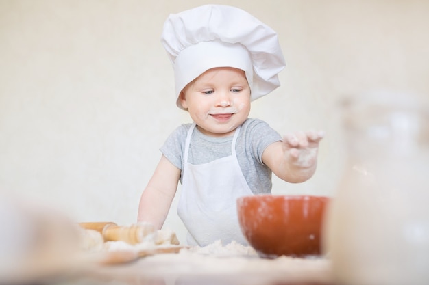 Der kleine Junge im Anzug des Kochs formt Teig Kleine Kinderjunge macht Abendessen im Kochanzug