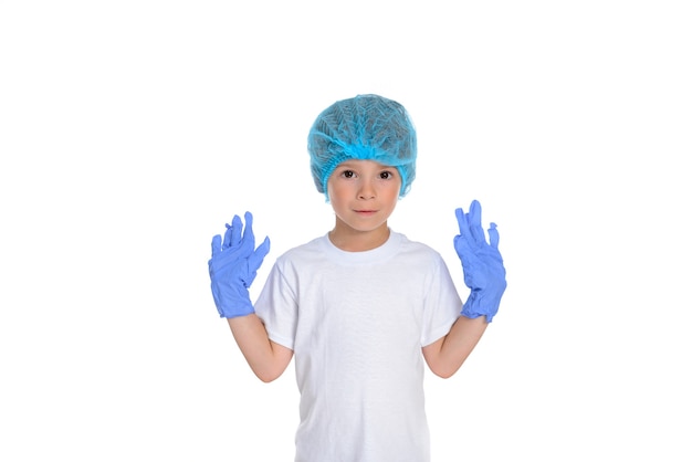 Der kleine Junge trägt ein weißes T-Shirt, eine medizinische Einwegkappe und blaue sterile medizinische Handschuhe.