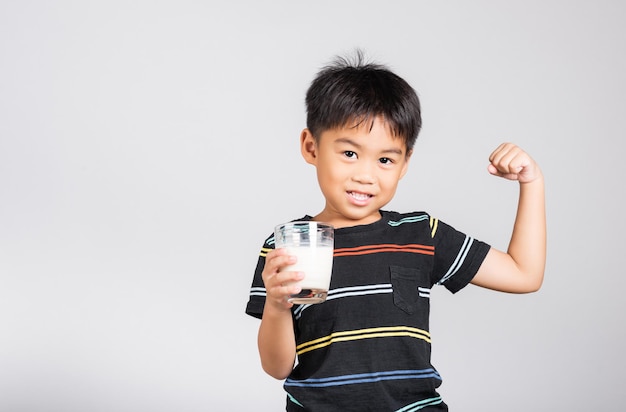 Der kleine süße Junge lächelt, hält Milchglas und zeigt eine starke Geste der Macht