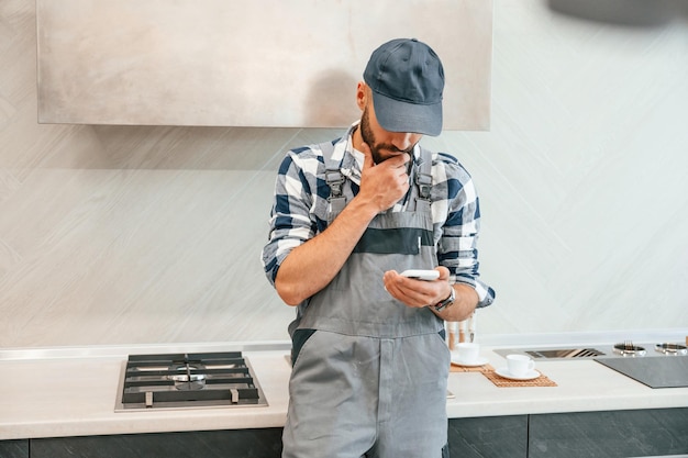 Der Klempner in Uniform hält das Smartphone in der Hand und ist zu Hause