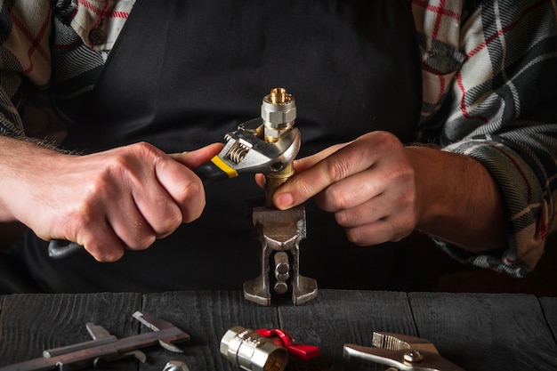Der Klempner verbindet die Messingbeschläge mit einem verstellbaren Schraubenschlüssel. Nahaufnahme eines Vorarbeiters ist Hände während der Arbeit in einer Werkstatt