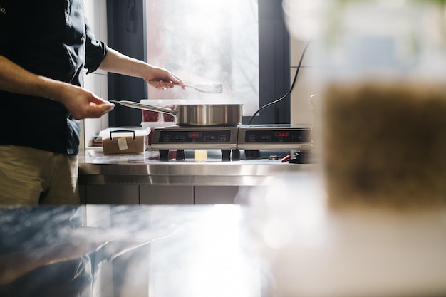 Der Koch arbeitet mit einem Induktionskochfeld Der Prozess des Bratens oder Schmorens in der Nähe