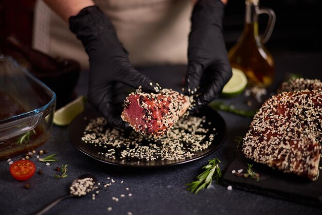 Der Koch bedeckt ein Stück Thunfischfilet vor dem Kochen mit Sesamkörnern