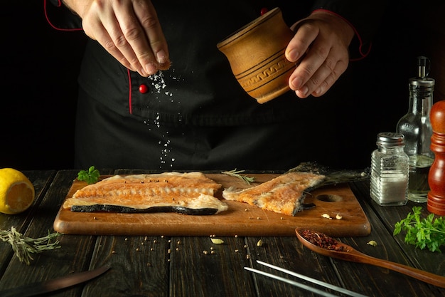 Der Koch bereitet frischen Lachs, Fisch, Forellen, Smorgus zubereitet und streut die Zutaten mit Salz