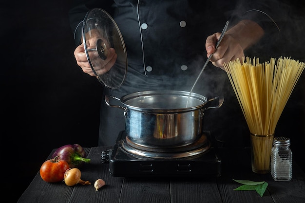 Der Koch bereitet italienische Nudeln in einem Topf mit Gemüse zu. Nahaufnahme der Kochhände beim Kochen in der Restaurantküche. Kostenlose Werbefläche.