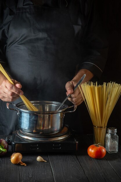 Der Koch bereitet italienische Nudeln in einem Topf mit Gemüse zu. Nahaufnahme der Kochhände beim Kochen in der Restaurantküche.