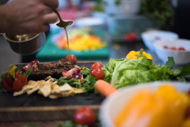 Der Koch fertigt die Steak-Fleischplatte von Hand mit dem abschließenden Dish-Dressing an und ist fast fertig zum Servieren am Tisch