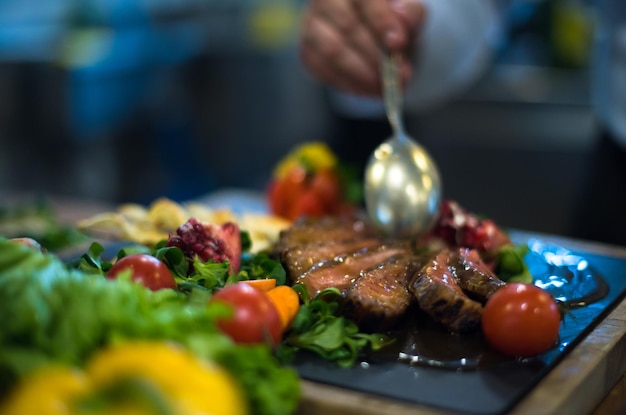 Der Koch fertigt die Steak-Fleischplatte von Hand mit dem abschließenden Dish-Dressing an und ist fast fertig zum Servieren am Tisch