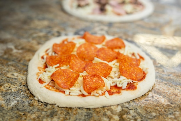 Der Koch fügt der Pizza mit Salami in der Pizzeria Schinken hinzu