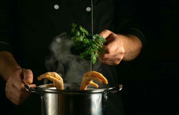 Der Koch fügt grünen Petersilie zu einem Topf mit kochenden Hühnerbeinen hinzu Konzept der Zubereitung köstlicher Suppe oder Brühe in der Küche eines Restaurants oder Hotels