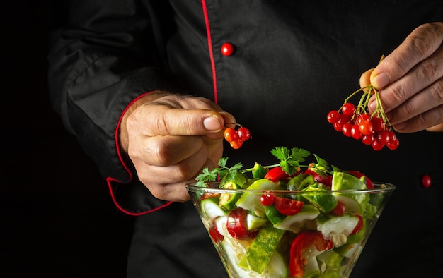 Der Koch fügt saftigem Viburnum zu vegetarischem Essen hinzu, bereitet mit den Händen eines Koch in der Küche einen köstlichen Salat vor, eine Menüidee für ein Hotel oder Restaurant