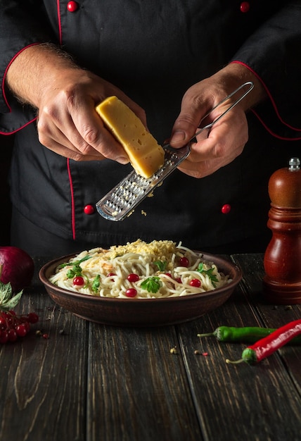 Der Koch fügt Spaghetti mit Gewürzen in einem Teller Menü oder Rezept für ein köstliches Mittagessen für ein Hotel oder Restaurant Hartkäse hinzu