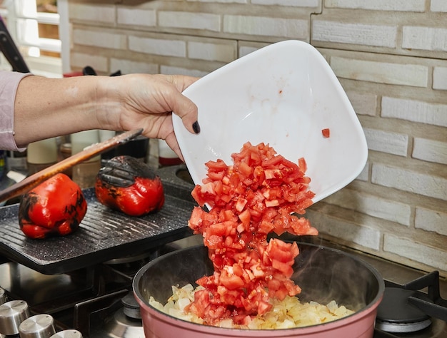 Der Koch gibt gehackte Tomaten in den Topf mit den Zutaten auf dem Gasherd