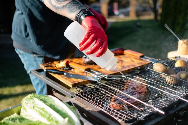 Der Koch gießt Wasser auf den Grill, um zu verhindern, dass das Fleisch anbrennt Konzept des korrekten Kochens von Fleisch im Freien