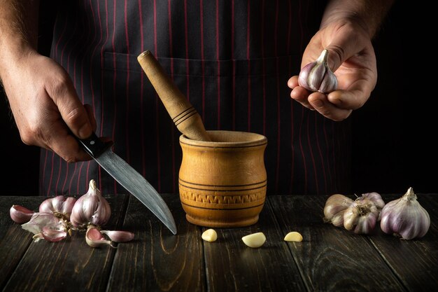 Der Koch hält den Knoblauch in der Hand, bevor er ihn in einem Mörtel zerkleinert Wir bereiten ein nationales Gericht vor.