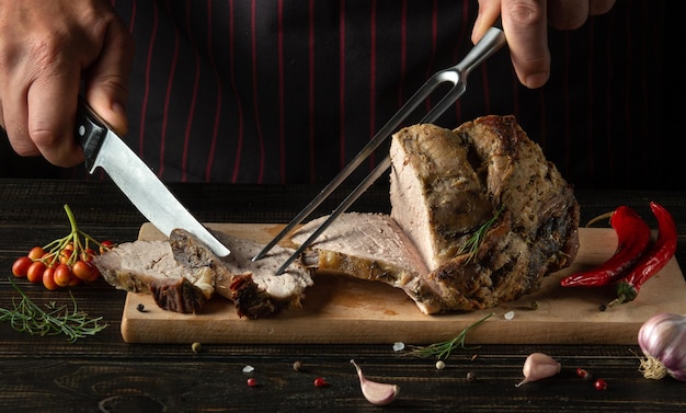 Der Koch mit Messer und Gabel schneidet ein Rindersteak auf einem Küchenschneidebrett Leckeres Mittagessen mit gebackenem Fleisch mit Gewürzen in einem Restaurant