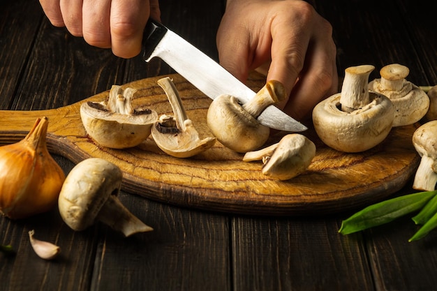 Der Koch schneidet Agaricus-Pilze auf einem Schneidebrett Nahaufnahme der Hände eines Küchenchefs mit einem Messer