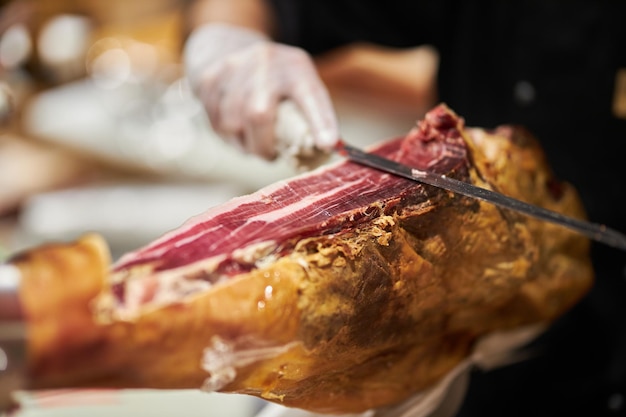 Der Koch schneidet das Jamon-Bild eines Schinkenschneiders mit einem Messer, das eine dünne Scheibe Schinken schneidet