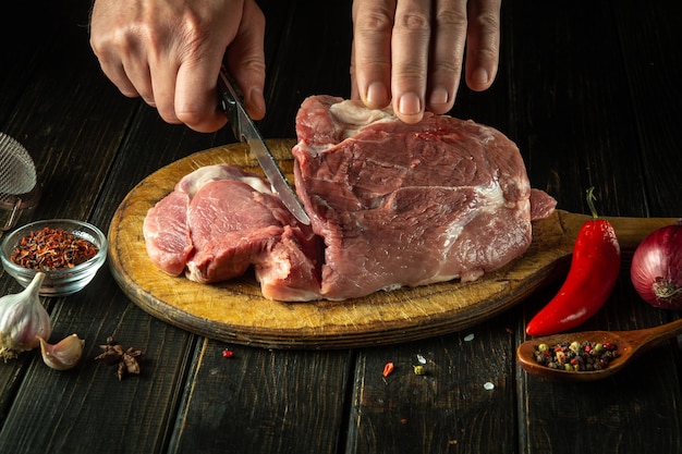 Der Koch schneidet ein rohes Rindersteak mit einem Messer auf einem Holzschneidebrett