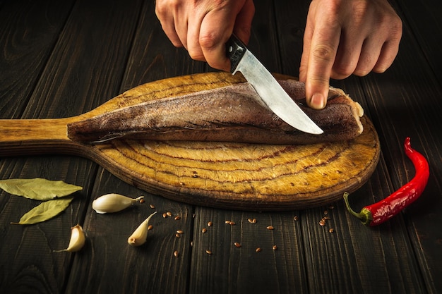 Der Koch schneidet mit einem Messer frischen Merluccius-Fisch auf einem Holzschneidebrett