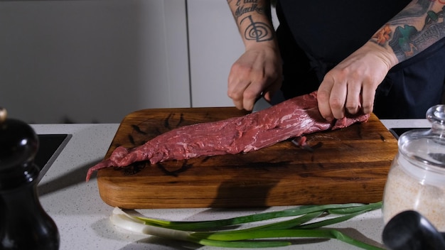 Der Koch schneidet Rindfleisch mit einem Messer auf einem Schneidbrett, der Koch trennt den Entrecotte von einem Stück frisches Fleisch.