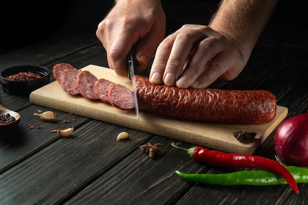 Der Koch schneidet Wurst auf einem Küchenschneidebrett Die Idee, leckere Sandwiches mit Gewürzen zuzubereiten