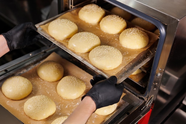 Der Koch steckt eine Backplatte mit gebackenen Burgerbrötchen in den Ofen