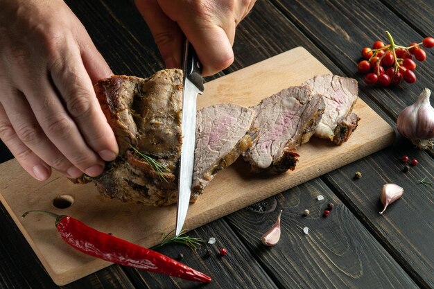 Der Koch übergibt das Schneiden von Rindersteak mit einem Messer auf einem Holzschneidebrett Draufsicht auf das Prozesskonzept der Lebensmittelzubereitung auf dunklem Hintergrund