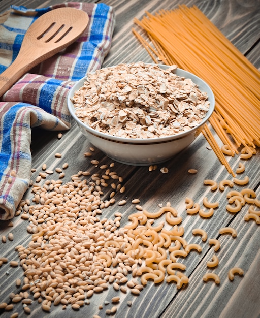 Der Kochvorgang. Eine Schüssel mit rohem Haferflocken, Müsli, Nudeln, Holzlöffel und einem Handtuch auf einem Holztisch. Vorbereitung des morgendlichen Frühstücks.