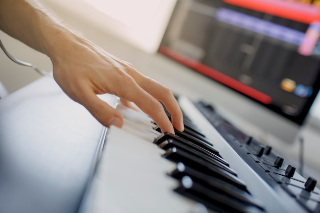 Der Komponist spielt die Klaviertasten im Tonstudio. Musikproduktionstechnologie, Mann arbeitet an Pianino und Computertastatur auf dem Schreibtisch. Nahaufnahme Konzept.