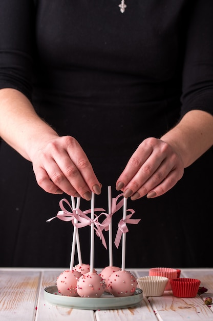 Der Konditor verziert Cake Pops mit Satinbändern. Desserts mit rosa Sahne.