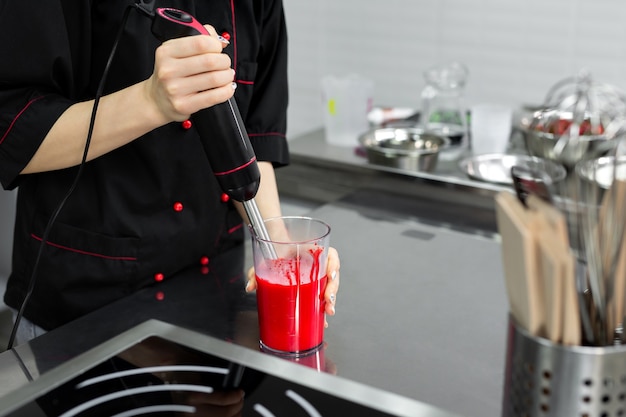 Der konditor zaubert mit einem mixer die rote spiegelglasur für den kuchen auf.