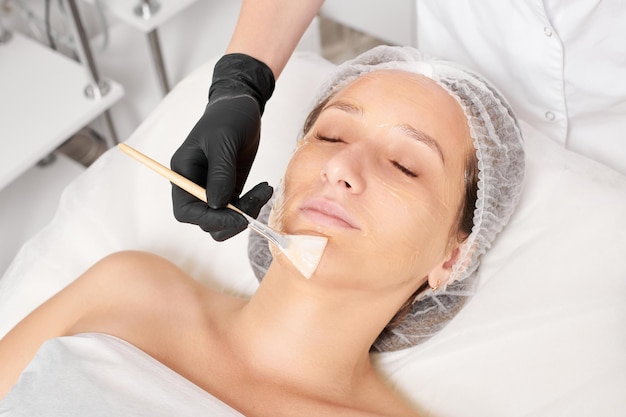 Der Kosmetiker trägt Honigmaske auf das Gesicht der Frau auf, um die Gesichtshaut im Beauty-Spa-Salon mit Feuchtigkeit zu versorgen