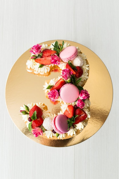 Der Kuchen mit Käsecreme und Honigkuchen ist mit Blumen, Beeren und Süßigkeiten dekoriert. Ein Kuchen in Form der Zahl 3.