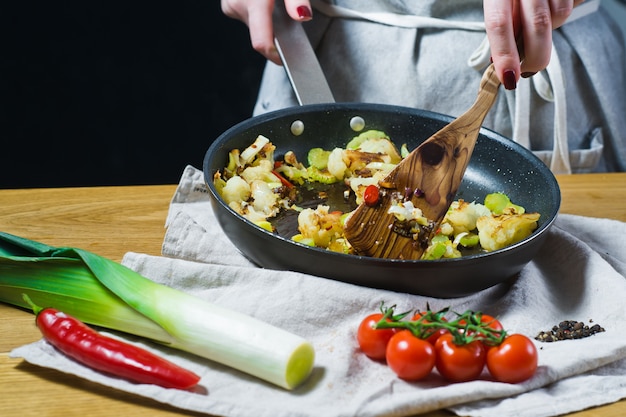 Der Küchenchef bereitet Blumenkohl und Lauch in einer Pfanne zu.