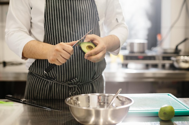 Der Küchenchef bereitet Essen zu Nahaufnahme eines männlichen Küchenchefs, der eine Avocado schält