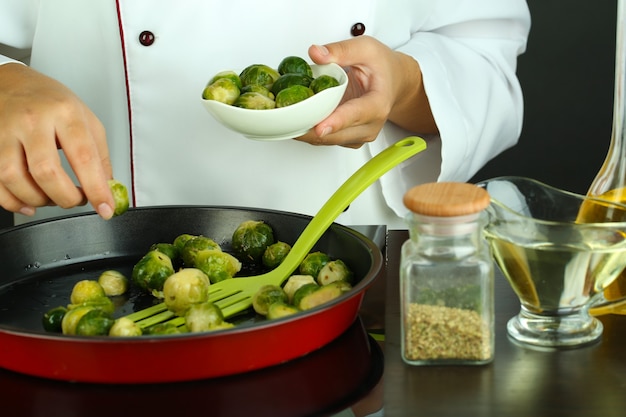 Der Küchenchef bereitet frischen Rosenkohl in einer Pfanne auf der Oberfläche der Kochfläche zu