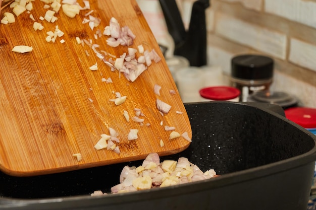 Der Küchenchef fügt eine Zwiebel zu einem Stück Rindfleisch hinzu, das in einer rechteckigen Pfanne über dem Gasherd gebraten wird. Französische Gourmetküche