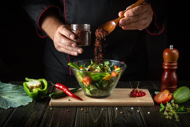 Der Küchenchef fügt vegetarisches Essen aromatische Gewürze hinzu Kochen Sie köstlichen Salat von den Händen des Kochs in der Küche Menüidee für ein Hotel oder Restaurant