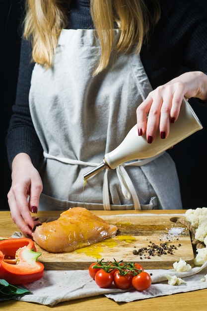 Der Küchenchef gießt Hähnchenbrust auf ein hölzernes Schneidebrett mit Olivenöl ein.